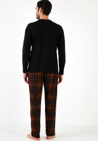 Camisa negra de manga larga con cuello redondo, combinada con pantalones de cuadros marrones que presentan acentos en blanco y negro, fabricados en una tela suave y con un ajuste relajado.