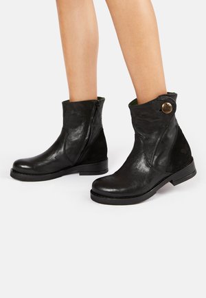 Bottines en cuir noir avec une fermeture éclair sur le côté, bout arrondi et petit talon. Elles disposent d'un col pliable et d'un accent de bouton décoratif.
