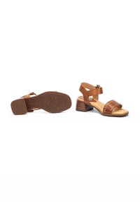 Sandalias de tacón de cuero marrón con dos correas, una ajustable. Suela de goma texturizada con patrón geométrico. Tacón bloque moderado.