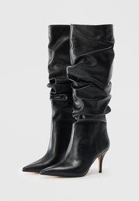 Black leather knee-high boots with a slouchy design, pointed toe, and a stiletto heel. Smooth texture and minimalistic construction.
