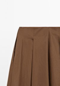 Jupe plissée marron avec fermeture éclair latérale, réalisée en tissu lisse, présentée sur un fond blanc.