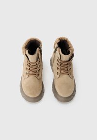 Bottines en suédine beige avec un col pelucheux, un laçage à l'avant, des zippers sur les côtés et des semelles en caoutchouc texturé.