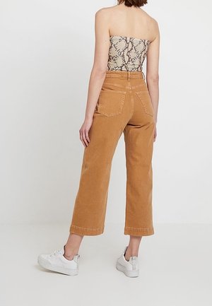 Bruine wijde jeansbroek van denim met een hoge taille, twee achterzakken en omgeslagen zoom, gecombineerd met witte sneakers.