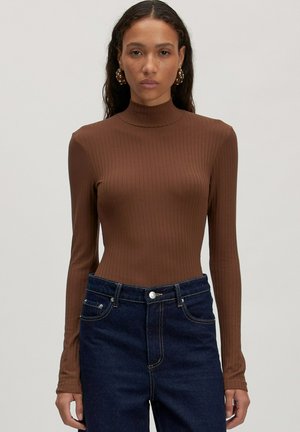 Bruine geribbelde longsleeve met hoge hals, gecombineerd met donkerblauwe spijkerbroek. De stof lijkt zacht en aansluitend.