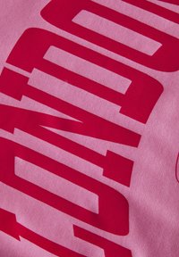 Un tissu rose présente un texte rouge audacieux et superposé avec des bords aigus et un design en couches, créant un contraste et un impact visuel significatifs.