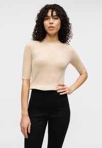 Μπεζ, πλεκτό τοπ με ριγέ υφή, κοντά μανίκια και στρογγυλή λαιμόκοψη, συνδυασμένο με μαύρο παντελόνι ψηλόμεσο. Λείου υφής και εφαρμοστή σχεδίαση.