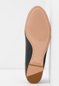 Semelle de chaussure en cuir noir avec une surface lisse et une texture striée, semelle extérieure en caoutchouc beige, arborant le logo 'Clarks'.