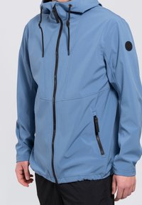 Chaqueta softshell azul claro con capucha, cierre frontal con cremallera y acentos negros en las cremalleras y el hombro. Cuerdas ajustables.