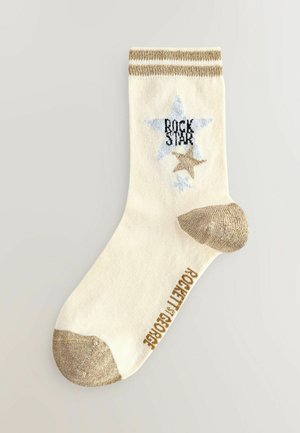 Crème sok met gouden accenten, met een blauwe ster en de tekst "ROCK STAR". Gouden teen en hiel, geribbelde boord. Textuurmateriaal.