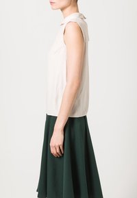 Lyse beige ærmeløs bluse med en foldet krave, parret med en mørkegrøn flagrende nederdel. Glat tekstur, minimalistisk design, rene linjer.