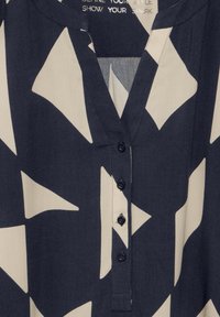 Marineblaue und cremefarbene Bluse mit geometrischen Mustern, V-Ausschnitt und Knopfleiste vorne. Weicher Stoff und glatte Textur mit einem locker sitzenden Design.