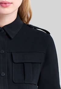 Czarna koszula z guzikami, z kołnierzykiem, dwoma przednimi kieszeniami i pagonami na ramionach, wykonana z gładkiego materiału o eleganckim designie.