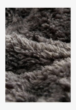 Sivkasta plišasta tkanina z globoko, mehko teksturo, ki vsebuje gosto pakirane, puhaste vlakne v različnih odtenkih sive, kar ustvarja otipno površino.