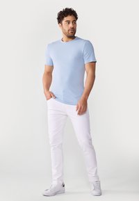 Tricou scurt, de culoare albastru deschis, cu mânecă scurtă, slim fit, asociat cu blugi albi, slim fit, și adidași albi. Design simplu, textură netedă, detalii minime.