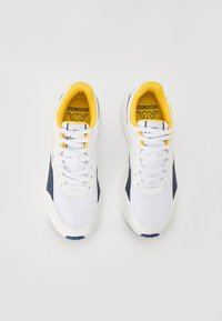 Baskets blanches avec accents navy, tige en mesh et synthétique, lacets blancs, col rembourré et doublure jaune vif. Semelle en caoutchouc pour l'adhérence.