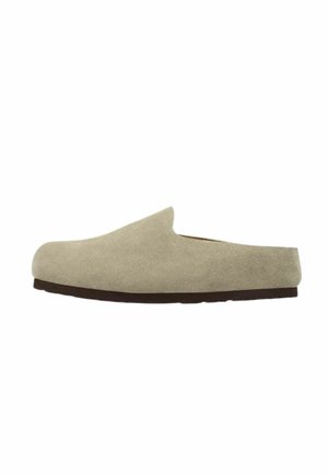 Zapato mule beige de ante sin cordones con tacón bajo y suela negra plana, mostrado de perfil sobre un fondo blanco.