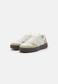 White and beige sneakers with a textured suede and smooth leather upper, round toe, and a dark rubber sole featuring a distinct pattern.
