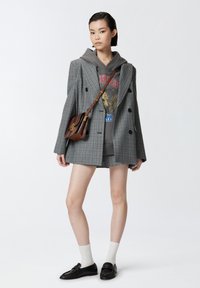 Blazer de cuadros gris de doble botonadura, sudadera gris con estampado gráfico, falda de cuadros, calcetines blancos, mocasines negros, pequeño bolso marrón.