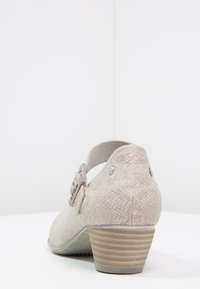Beżowe buty na niskim obcasie o teksturowanym, wężowym wykończeniu. Posiadają klamrę i pasek oraz paskowy wzór obcasa. Miękki, matowy materiał.