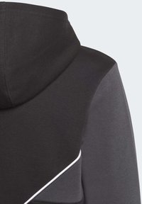 Huvtröja med en svart överdel och grå nederdel, med kontrasterande vit piping längs sömmen. Mjuk tygtextur.