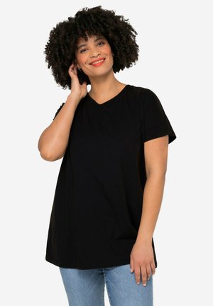 Zwarte, kortemouw V-hals T-shirt van zacht stof; comfortabele pasvorm met zichtbare naden. Gecombineerd met lichtblauwe jeans.