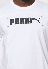 Camiseta blanca de algodón con el texto y logo en negro de "PUMA" en un diseño audaz, con cuello redondo y mangas cortas, de textura suave.