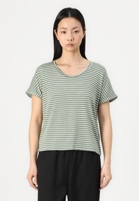 Grünes gestreiftes T-Shirt mit kurzen Ärmeln, rundem Ausschnitt und aufgerollten Ärmeln, aus einem weichen Material. Kombiniert mit schwarzen Hosen.