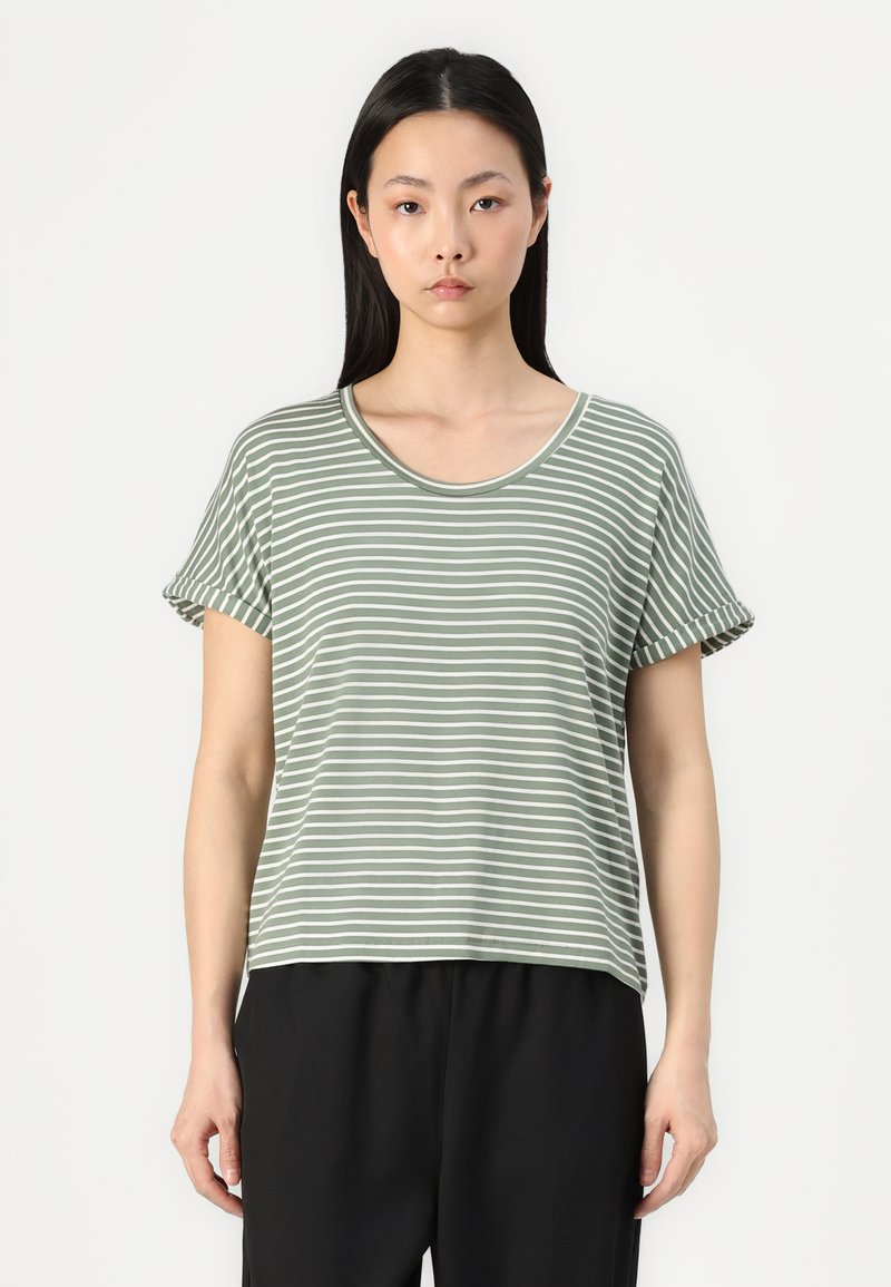 T-shirt de manga curta em verde às riscas, com decote redondo e mangas enroladas, feita de um tecido suave. Combinada com calças pretas.