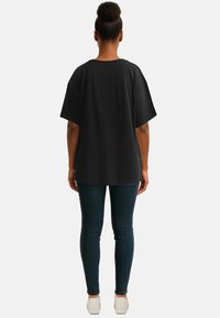 T-shirt nera oversize con maniche corte, scollatura rotonda e texture liscia, abbinata a jeans skinny scuri e sneakers bianche.