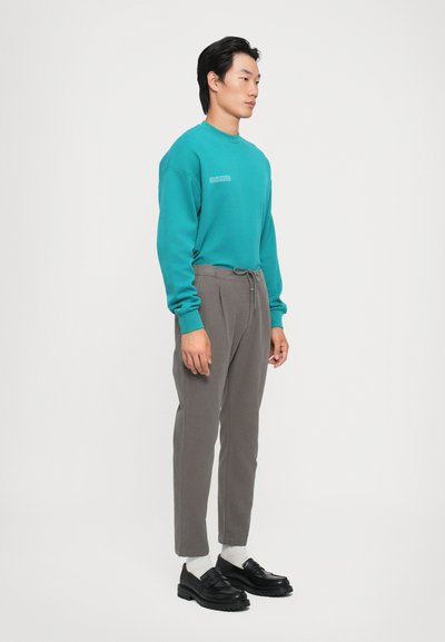 Turquoise sweatshirt with a crew neckline and small white text on the chest, paired with gray tapered pants and black loafers.