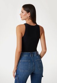 Bodysuit negro sin mangas combinado con jeans de denim azul de talle alto, que presentan un diseño clásico de cinco bolsillos y una etiqueta tejida en la parte trasera.