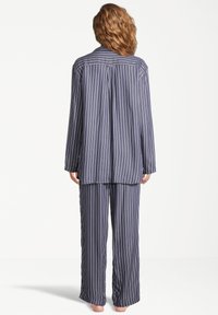 Marinrandig pyjamasett med en knäppning på toppen, långärmar, löst sittande byxor och mjukt tyg.