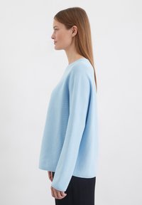 Pull léger bleu, texturé, avec un col rond, des manches longues et une coupe décontractée, présenté sur un modèle de profil.