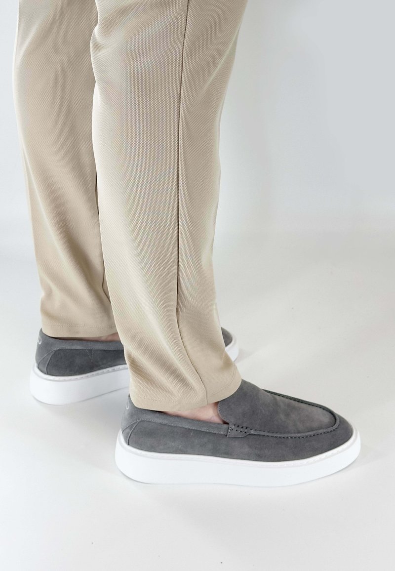 Grijze suède instappers met witte rubberen zolen, voorzien van gestikte details en een gladde textuur, gecombineerd met beige textuur-pantalon.