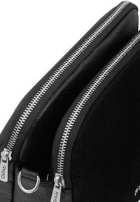 Bolso negro con cremallera con cuero texturizado y un exterior suave. Accesorios en plata incluyen cremalleras y un detalle en forma de D.