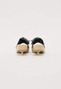 Τζιν ανοιχτού μπροστά κλειστού τύπου παπούτσια με πλέκτο μπεζ πάτο, διαθέτοντας διαφανή πλαστική φτέρνα και ιμάντα στο πίσω μέρος για επιπλέον στήριξη.