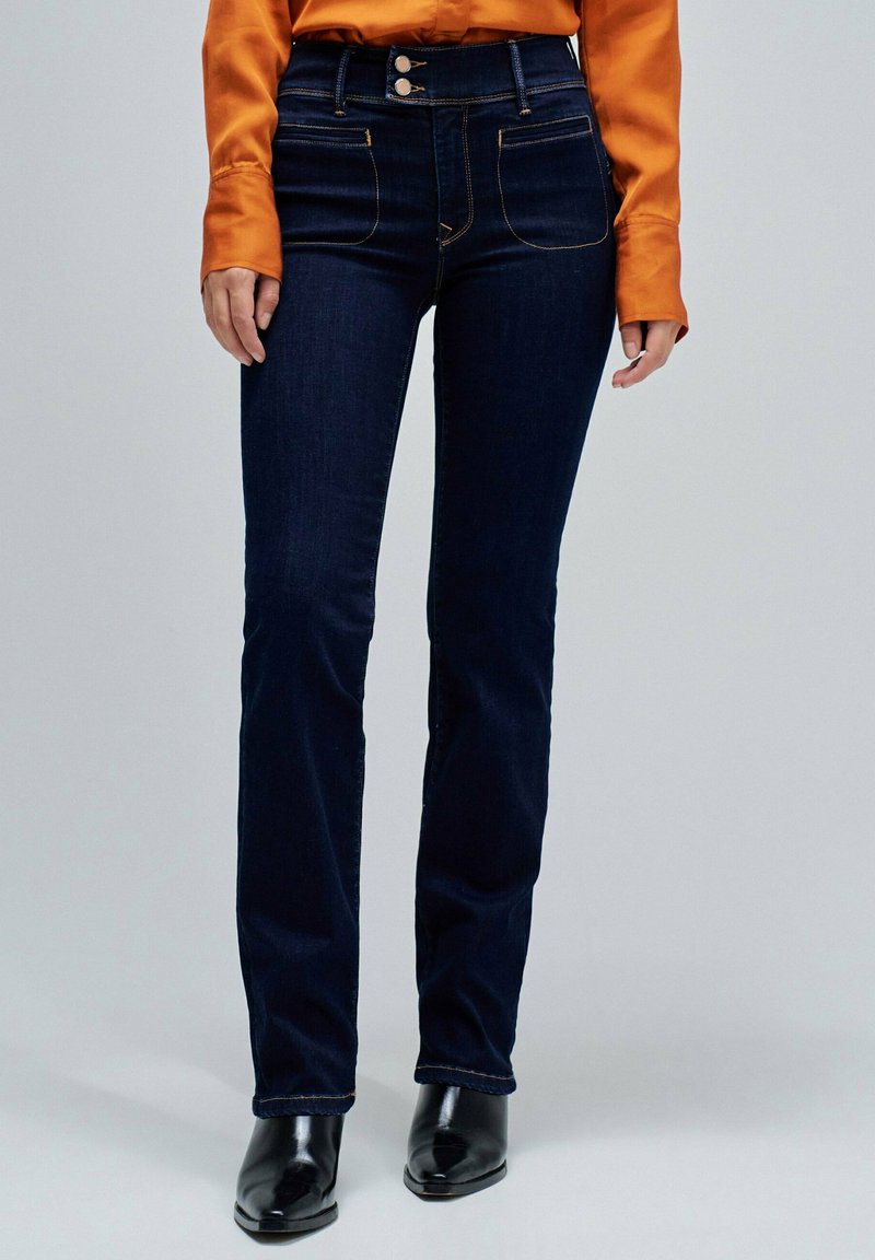 Jeans de tiro alto azul oscuro con un corte ajustado, que cuentan con dos bolsillos frontales, costura visible y detalles en botones plateados.