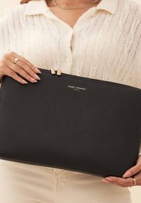 Clutch in pelle nera con texture granulosa, zip in metallo dorato e nome del marchio "ISABEL BERNARD, PARIS" in rilievo sul davanti.