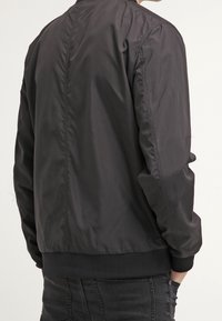 Black bomber jacket made of lightweight, smooth fabric. Features ribbed cuffs and hem, with a minimalist design and no visible patterns.