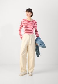 Red and white striped long-sleeve shirt, cream wide-leg pants, holding a light blue denim jacket, and wearing white sneakers.