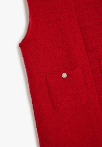 Rote gewebte Weste aus strukturiertem Stoff, mit zwei vorderen Taschen und einem dekorativen Perlenknopfakzent. Ohne Ärmel; lässiges, gerades Design.