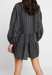 Vestido negro y blanco con estampado, mangas abullonadas, dobladillo con volantes en capas y una tela texturizada que presenta rayas verticales y acentos de puntos.