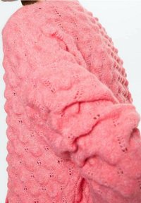 Suéter de punto rosa con un patrón texturizado, que presenta un diseño acanalado en las mangas y un ajuste ligeramente holgado.