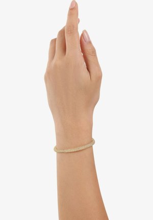Pulsera bangle de tono dorado con un acabado liso y texturizado, llevada en una mano de piel clara, que presenta un diseño circular y delgado.