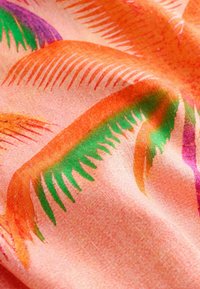 Gros plan sur un tissu avec un fond rose et des motifs abstraits de feuilles tropicales dans des tons orange, vert et violet.