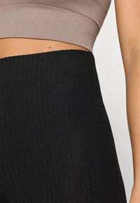  Sorte ribbede leggings med en høj talje, der glider blødt over til en tætsiddende tekstur, parret med en dæmpet brun crop top.