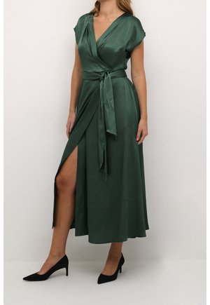 Green satin wrap dress with short sleeves, a side slit, and a belt at the waist. Black high-heeled shoes complement the outfit.
