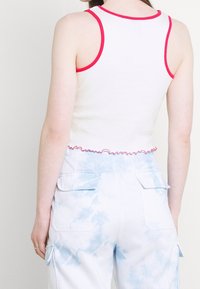 Vit ribbad ärmhlösa tröja med röd kant och volangves, ihop med ljusblå tie-dye cargobyxor som har sidofickor och klaffdetaljer.