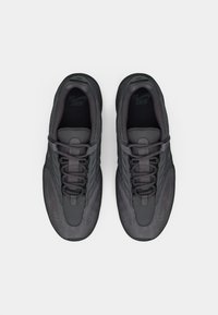 Μαύρα αθλητικά παπούτσια με υφασμένο συνθετικό επάνω μέρος, στρογγυλεμένη μύτη, δέσιμο με κορδόνια και μαξιλαρωμένο γιακά. Μινιμαλιστικό στυλ με διακριτική εταιρική σήμανση.