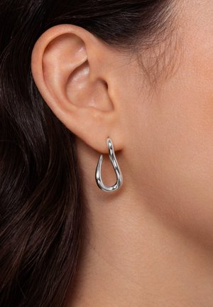 Boucles d'oreilles en argent en forme de goutte lisse et polie, pendantes sous le lobe de l'oreille, mettant en valeur leur forme fluide et leur design moderne.